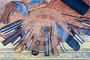 Leather craft tools on a wooden background. Leather craftmans work desk . Piece of hide and working handmade tools on a work table