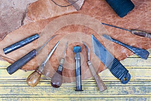 Leather craft tools on a wooden background. Leather craftmans work desk . Piece of hide and working handmade tools on a work table