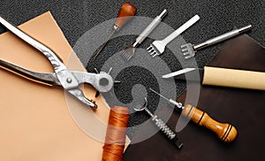 Leather crafting DIY tools lies on natural black and brown leather.