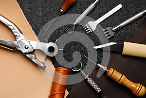 Leather crafting DIY tools lies on natural black and brown leather.