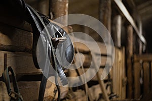 leather horse saddle hanging on a fence in a stable with space for text