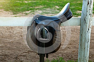 Leather horse saddle on wooden fence.