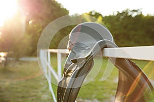 Leather horse saddle on wooden fence outdoors