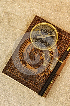 Leather journal notebook with a fountain pen and antique compass in sand.