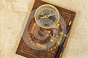Leather journal notebook with a fountain pen and antique compass in sand.