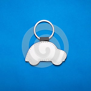 Leather key ring in car shape on blue paper background. Blank key chain for your design