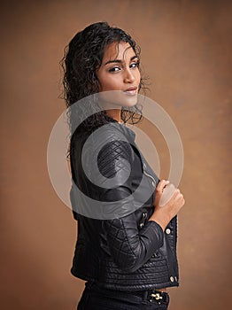 The leather look. Studio shot of an attractive young woman in a leather jacket against a brown background.