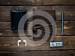 leather notebook with a metal ballpoint pen  wallet  headphone and a pocket multitool on wooden background