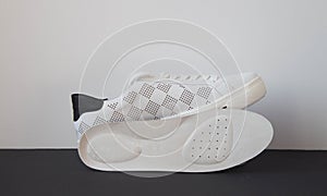 Leather orthopedic insole and white sport shoe on black white background.