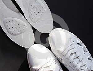 Leather orthopedic insoles and white sports shoes on black background.