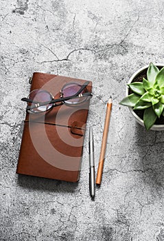 Leather personal organizer, pen, pencil, glasses and succulent flower on a gray table, top view