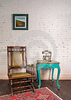 Leather rocking chair, wooden green vintage table and antique golden telephone set over bricks wall