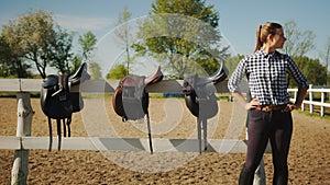 Leather Saddles Hanging On The Wooden Fence In The Sandy Arena - Girl Posing