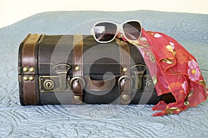 Leather vintage suitcase with tropical scarf and sunglasses draped on top, travel concept