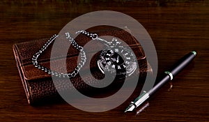 Leather Wallet with Pocket Watch and Fountain Pen on a Wooden Table Top