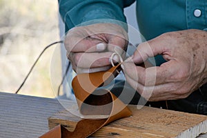 Leather work: craftsman threads trim into holes on a leather belt. view 3