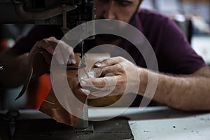 Leather work in progress: skilled craftsman sewing brown leather piece with industrial sewing machine