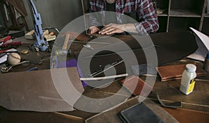 Leather worker man sitting behind table with tools and holds leather key case