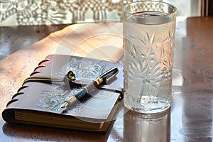 a leatherbound journal, fancy pen, and a tall glass of water on the table photo