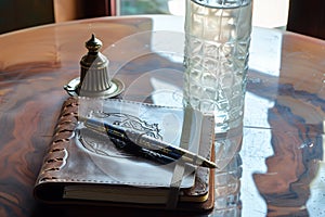 a leatherbound journal, fancy pen, and a tall glass of water on the table photo