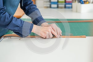 Leatherworker measuring and cutting leather in workshop.