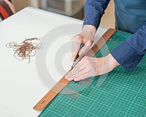 Leatherworker measuring and cutting leather in workshop.