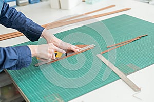Leatherworker measuring and cutting leather in workshop.