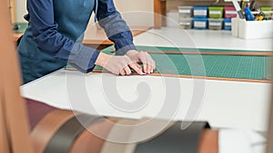 Leatherworker measuring and cutting leather in workshop.