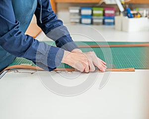Leatherworker measuring and cutting leather in workshop.