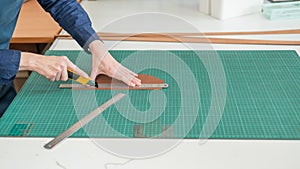 Leatherworker measuring and cutting leather in workshop.