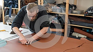 Leatherworker measuring and cutting leather in workshop.