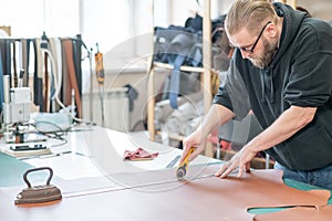 Leatherworker measuring and cutting leather in workshop.