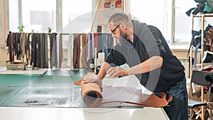 Leatherworker unrolls rolls of leather in workshop.