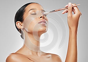 Leave me be to my beauty. Studio shot of an attractive young woman applying makeup to her face with a brush against a