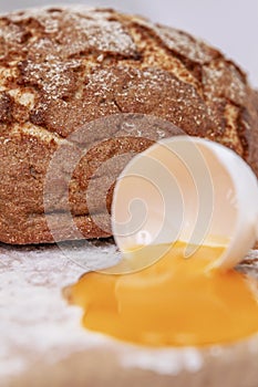 A leavened self-made brown bread covered in flour in the background of shot. Spilled egg yolk in the foreground