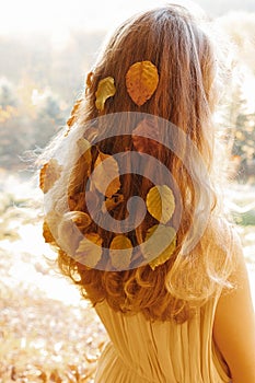 Leaves in the hair of a woman walking on a warm autumn day in the forest