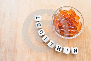 Lecithin gel pills in a round glass bowl and with the word Lecetin from the letters of cubes on a light wooden background. Soy
