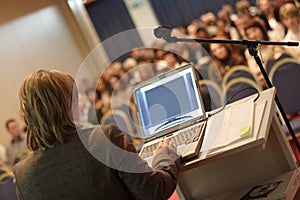 Donna d'affari a podio con il computer portatile di docenza pubblico in auditorium.