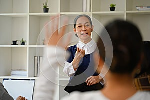 Lecturer pointing at female student sitting with hand raised while asking the question in the classroom