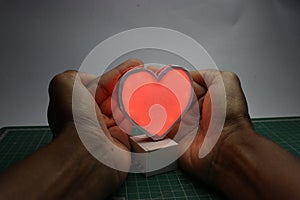 LED heart made using 3D print technology being covered with hands showing the concept of protected love