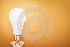 LED lamp twisted out of a socket on an orange background with copy space: energy-saving concept and Earth Hour