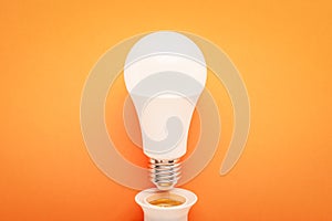 LED lamp twisted out of a socket on an orange background: energy-saving concept and the hour of the earth