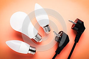 LED lamps and electrical plug on an orange background: the concept of energy saving and Earth Hour