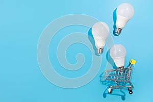 Led lamps in shopping car on isolated blue background. Flat lay. Concept ecology, save planet earth