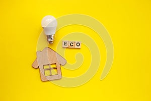 LED light bulb and wooden house on yellow background with copy space. Top view, flat lay. Energy eco and save concept