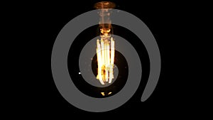 LED Retro-Style Light Bulb Hanging on Wire and Flickering on Black Background