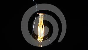 LED Retro-Style Light Bulb Hanging on Wire and Flickering on Black Background
