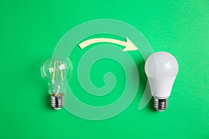 LED and simple light bulbs with arrow on green background, flat lay. Energy saving concept