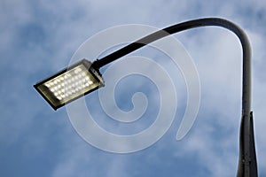 LED street lamp glowing on background of blue sky with clouds