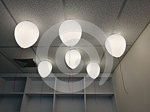 LED white creamy balloons burning fly away in the sky at night in the office room with blur white wood shelf background, holiday c